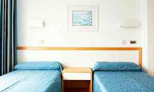 Två enkelsängar med blåa överkast och en träpanel bakom. (AI-genererad text)