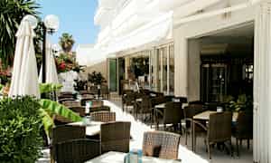 Utomhusservering med mörka rottingstolar och vita bord, omgiven av grönska. (AI-genererad text)