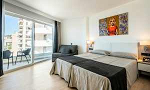 Ett hotellrum med två enkelsängar, en soffa, en balkong och stora glasfönster. (AI-genererad text)