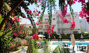 En byggnad med flera balkonger bakom hängande rosa blommor, en simbassäng och solstolar. (AI-genererad text)