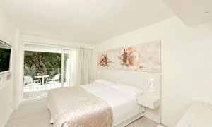 Ett ljust hotellrum med en dubbelsäng, väggdekoration med motiv av snäckor och ett balkongområde utanför glasdörrarna. (AI-genererad text)