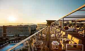 En takbar med sittplatser och bord vid solnedgången, med utsikt över en pool och byggnader. (AI-genererad text)