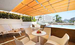 En utomhusterrass med solstolar, bord och stolar. Det finns en liten pool och utsikt mot hotellbyggnader. (AI-genererad text)