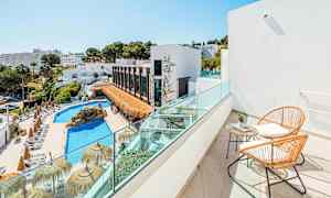 Utsikt från en balkong med två stolar och ett bord mot en pool och byggnader omgivna av grönska. (AI-genererad text)