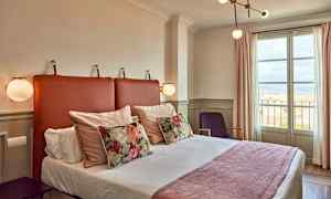 Ett hotellrum med en säng, dekorativa kuddar och ett fönster som visar utsikt. (AI-genererad text)