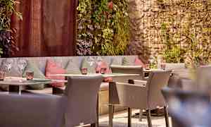 En uteservering med sittplatser och dekorerade väggar, omgiven av grönska. (AI-genererad text)