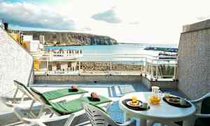 Terrass med två solsängar och en bord med orangejuice och bakverk, havsutsikt i bakgrunden. (AI-genererad text)