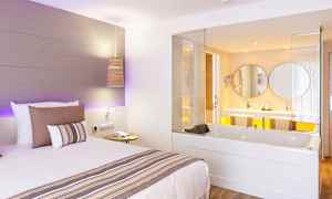 Hotellrum med en säng och en inbyggd badtunna som vetter mot ett badrum. (AI-genererad text)