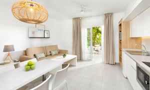 Ett ljus och modernt möblerat rum med en beige soffa, vitt matbord och kök, samt öppna dörrar till en möblerad balkong. (AI-genererad text)