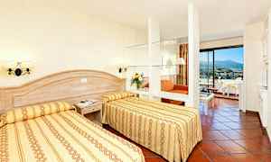 Ett hotellrum med två enkelsängar, en sittgrupp och balkong. (AI-genererad text)