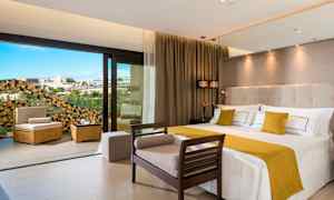 Ett modernt hotellrum med en stor säng och sittmöbler, samt en öppning mot en balkong med utsikt. (AI-genererad text)