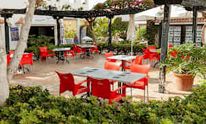 Uteservering med röda stolar och bord, omgiven av grönska. (AI-genererad text)