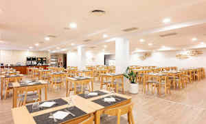 En matsal med träbord och stolar. Rummet är ljus och rymligt med dukar och uppsatta glas. (AI-genererad text)