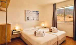 Ett ljust hotellrum med en dubbelsäng, fönster med utsikt över landskapet och en väggmålning ovanför sängen. (AI-genererad text)