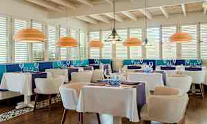 En elegant restaurang med vita dukar, blå dekor och moderna taklampor. (AI-genererad text)