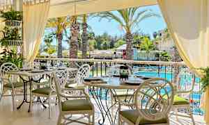 En restaurang med vita bord och stolar, utsikt över palmer vid en pool. (AI-genererad text)