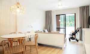 Ett ljust och modernt inrett vardagsrum med ett matbord, en soffa och en barnvagn vid glasdörren. (AI-genererad text)