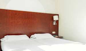 Två enkelsängar med vita sängkläder och en mörk trä huvudgavel. En vägglampa är monterad på sidan. (AI-genererad text)