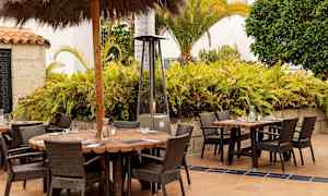 Utomhus sittgrupper med träbord och rottingstolar framför en växtbeklädd bakgrund. (AI-genererad text)