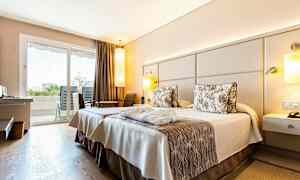 Hotellrum med två sängar och inredning i neutrala toner. Utsikt mot balkong genom glasdörrar. (AI-genererad text)