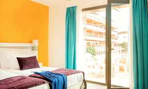 Ett hotellrum med en säng, färgglada kuddar och textilier, samt en glasdörr som leder till en balkong. (AI-genererad text)