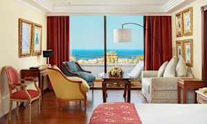 Rum med röda gardiner, möbler och utsikt över havet. (AI-genererad text)