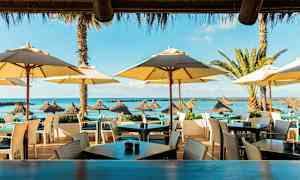 Uteservering vid stranden med parasoller och utsikt mot havet. (AI-genererad text)