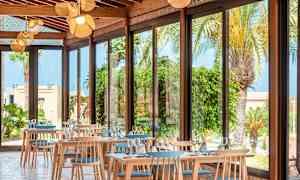 En restaurang med stora fönster och utsikt över palmer och växter. (AI-genererad text)