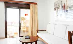 Interiör av ett rum med en soffa, ett bord och en målning av segelbåtar på väggen. Glasdörr leder till en balkong. (AI-genererad text)