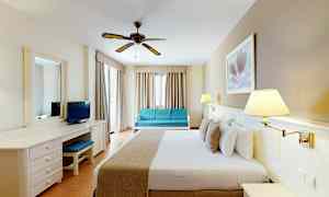 Ett hotellrum med en dubbelsäng, skrivbord, soffa och takfläkt. (AI-genererad text)