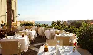 Bild på en utomhusrestaurang med dukade bord och havsutsikt. (AI-genererad text)