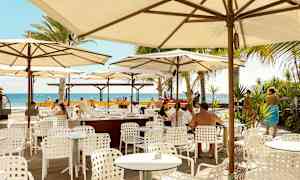 Utomhusrestaurang med vita bord och stolar under parasoller, utsikt mot havet. (AI-genererad text)