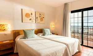 Två enkelsängar med vita sängkläder i ett rum med utsikt mot en balkong. (AI-genererad text)