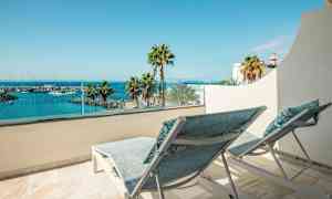 Två solstolar på en balkong med utsikt över en hamn och havet. (AI-genererad text)