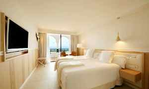 Ett hotellrum med två bäddar, en väggmonterad TV och en balkong med utsikt över havet. (AI-genererad text)