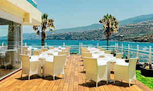 Utomhusterrass med matbord och stolar, utsikt över havet och omgivande landskap. (AI-genererad text)