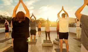 En grupp människor utför yogapositioner på en utomhusplattform vid solnedgången. (AI-genererad text)