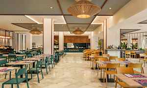 En matsal med bord och stolar, i vilken en kock syns arbeta vid en matstation. (AI-genererad text)