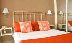 Ett hotellrum med en säng klädd i vita och röda sängkläder, omgivna av vägglampor. (AI-genererad text)