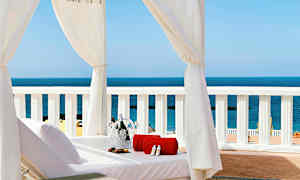 Solbädd under vit baldakin med utsikt över havet, med handduk och champagnekyl. (AI-genererad text)