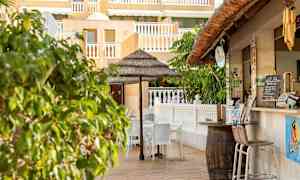 Uteservering med stolar och ett parasoll i närheten av en byggnad med gult fasad och vita räcken. (AI-genererad text)