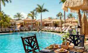 Frukost serverad vid ett bord intill en pool med solstolar och parasoller i bakgrunden. (AI-genererad text)