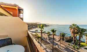 Utsikt från en balkong mot en palmkantad strandpromenad och havet under en klar himmel. (AI-genererad text)