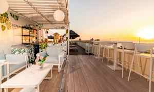 En solig takterrass med stolar, bar och bord, samt solnedgång i bakgrunden. (AI-genererad text)