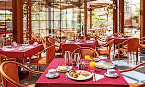 En restaurang med bord klädda i röda dukar, serverar frukost inklusive kaffe, juice och bakverk. (AI-genererad text)