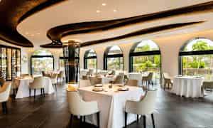 Restaurang med ljus inredning, stora fönster, och dukade bord. (AI-genererad text)