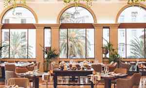 Ett elegant inrett matsal med stora bågformade fönster som vetter mot en grönskande utsikt med palmer. (AI-genererad text)