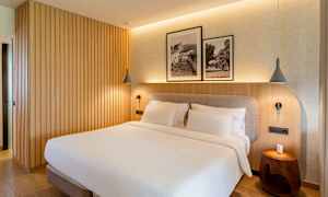 Ett sovrum med en dubbelsäng, träpanelvägg och två inramade svartvita fotografier ovanför sängen. (AI-genererad text)