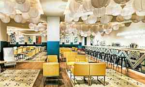 En modern och inbjudande restaurang med gula fåtöljer, dekorativa lanternor i taket och en stilren bar. (AI-genererad text)