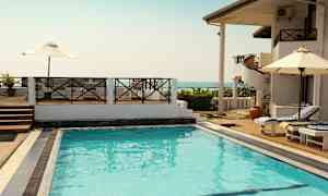 Utomhuspool vid ett semesterkomplex med solsängar och parasoller samt utsikt över havet. (AI-genererad text)